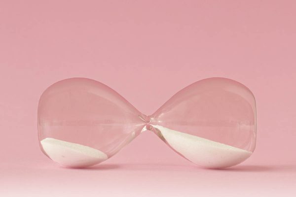 Hourglass lying on pink background – Concept of time and woman