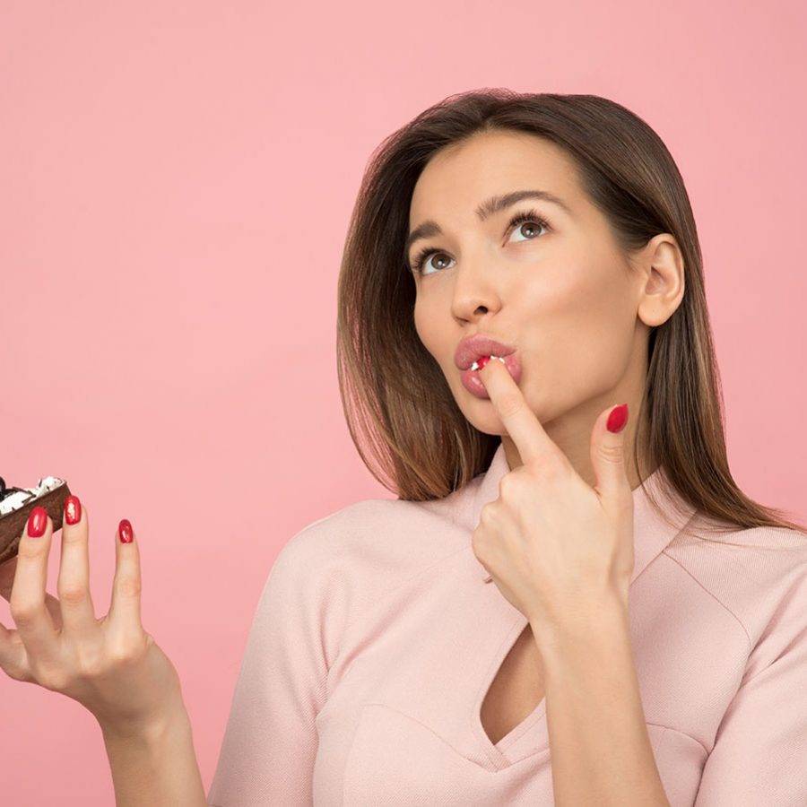 woman-eating-cupcake-while-standing-near-pink-background-1036621